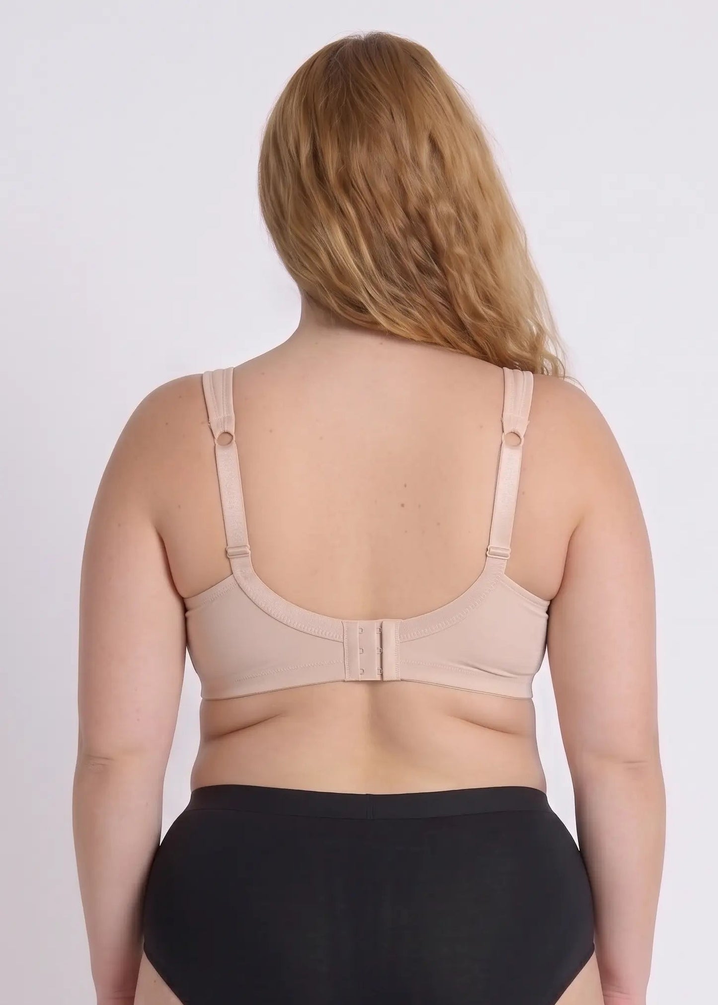 Back view of a model wearing a beige bra for full busts, showing the wide smoothing back band and adjustable comfort straps with ring details.