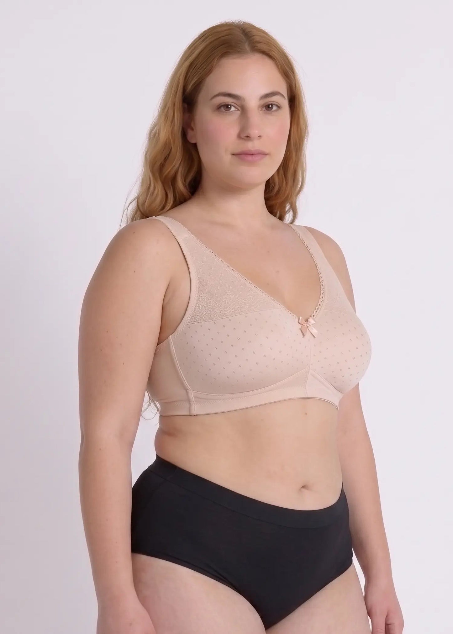 Three-quarter view of a model wearing a comfortable beige everyday bra for large busts, featuring a delicate dotted pattern, lace trim, and a small center bow.