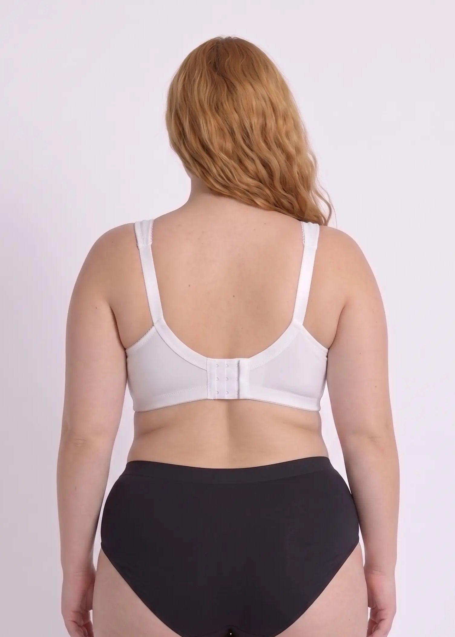 Back view of a model with a full bust wearing a supportive white bra, featuring a wide back band with hook-and-eye closures and wide adjustable straps.