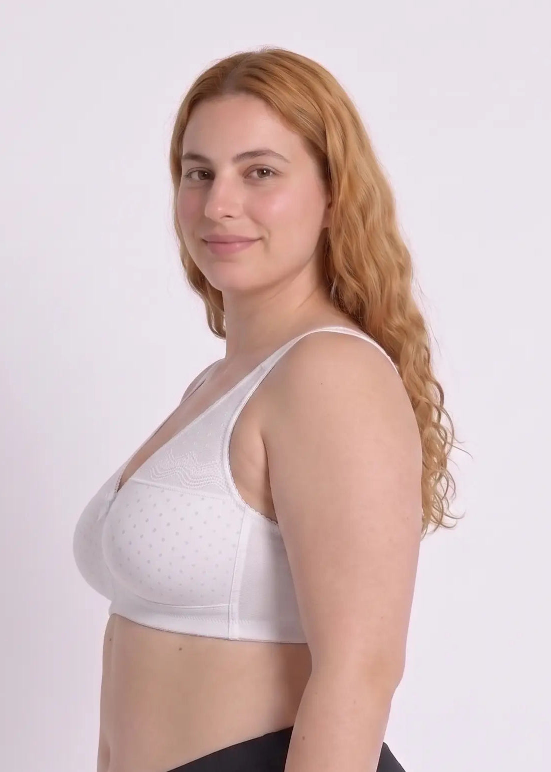 Side profile view of a model wearing a comfortable white wireless bra with dotted detailing, demonstrating smooth side coverage and support for a full bust