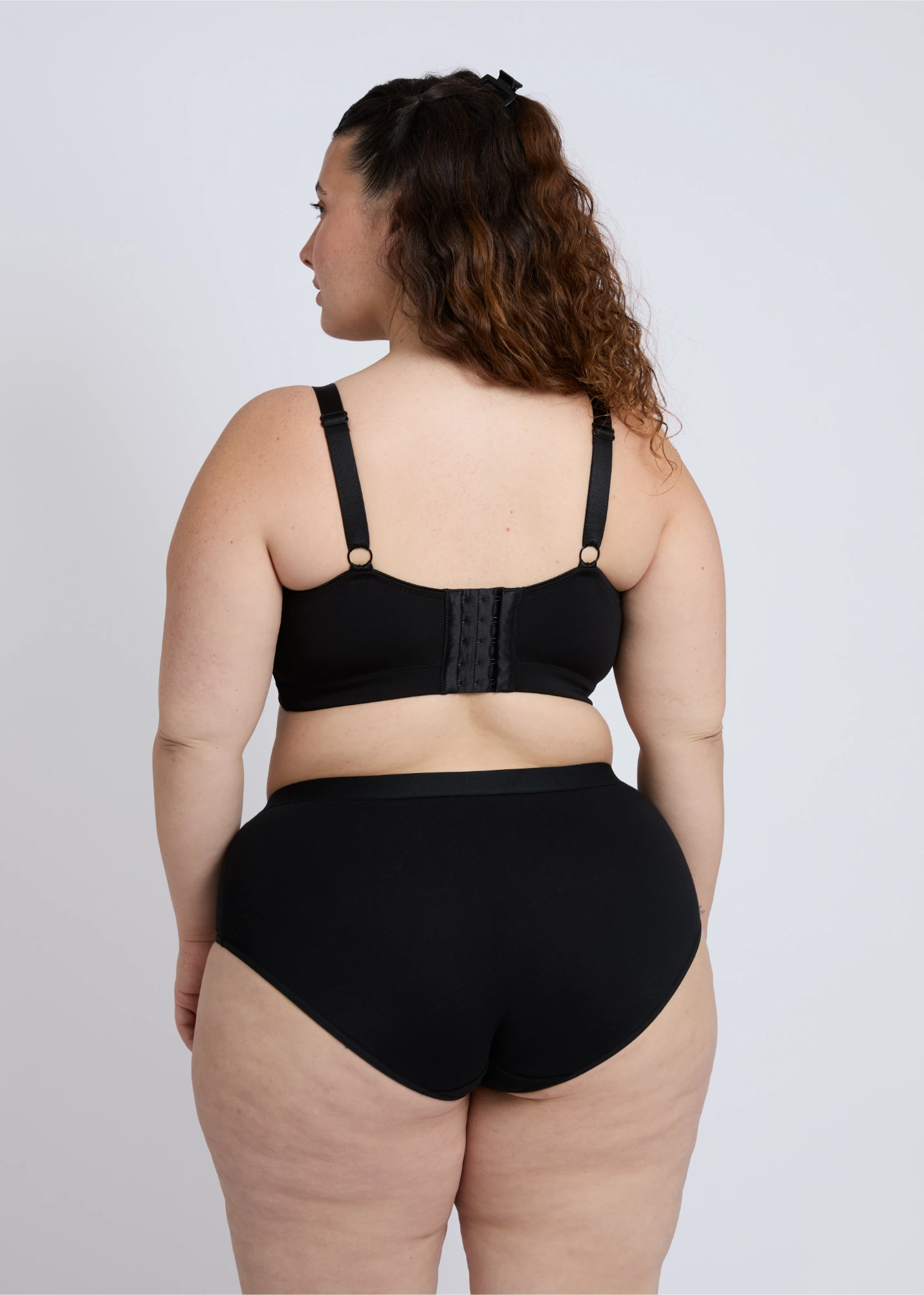 Back view of the black Joy seamless wire-free bra for large breasts on a plus-size model, showcasing the smooth seamless back band, adjustable straps, and supportive closure