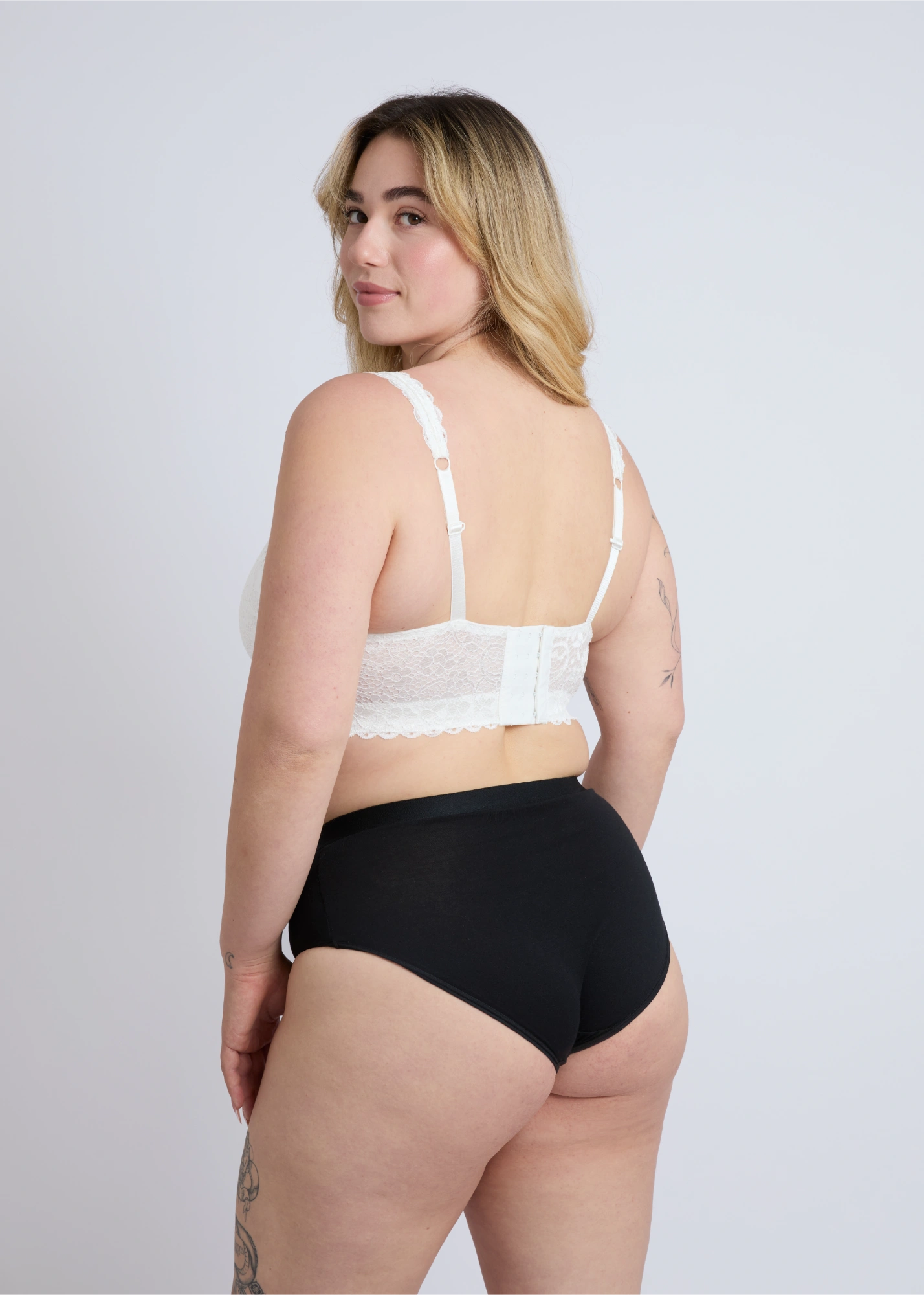A back view of the white Kimi wire-free lace bra for large breasts on a plus-size model, showcasing the wide lace band, adjustable straps, and supportive fit