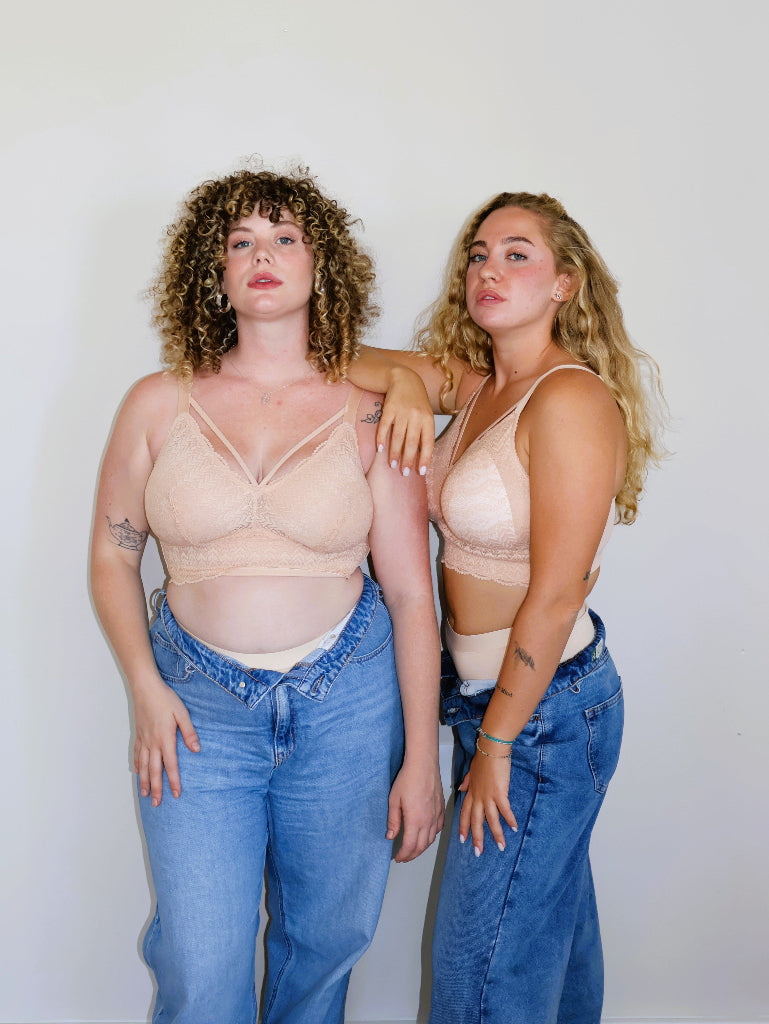 Two inclusive plus-size models with large breasts posing in matching nude (peach-toned) wire-free lace bralettes (Mia bra) and open blue jeans against a neutral background, showcasing comfort and supportive fit